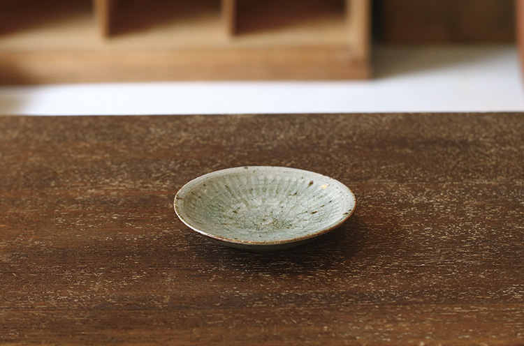 灰を使った釉薬を用いて、ガラスのような光沢のある質感に。小さ い豆皿だけど、焼き物ならではの魅力を凝縮した一皿。白く文様を浮き出させる「三島手」という技法で作られている。2,160円