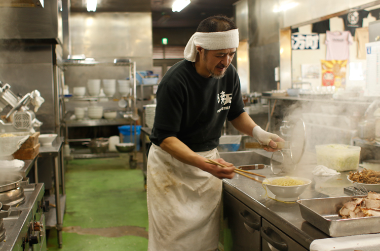 広い厨房で仕事する細貝大将。包丁切り麺を大鍋で泳がすように茹で、強靭なコシと モチモチ食感を生み出す