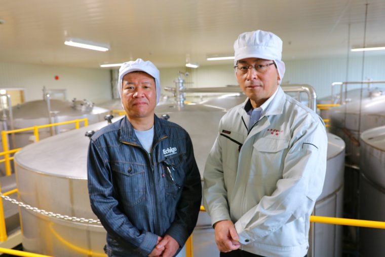 阿部社長（右）と、エチゴビール創業以来製造に携わる管理部の小林課長（左）。背後の巨大なタンクはビール発酵用タンクです