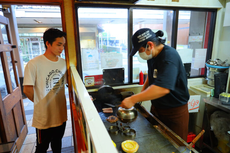 調理風景をわくわくした表情で見つめる坪田さん。右は店主の遠藤和彦さん