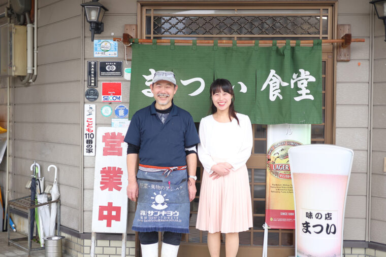 店主・松井良孝さんと松本栞奈さんをのれんの前でパチリ