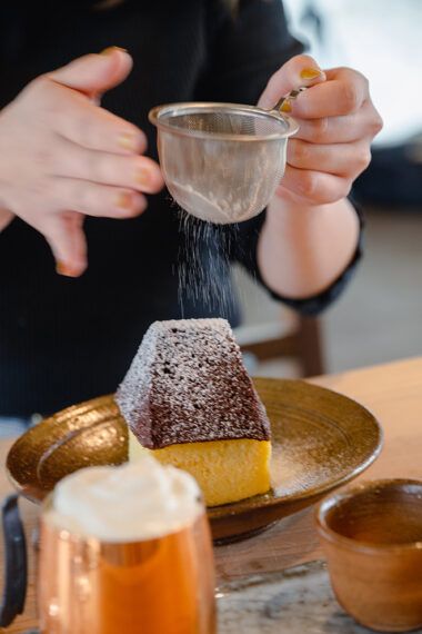 かやぶき屋根の建物をモチーフにしたシフォンケーキに、雪（粉糖）を降らせてから味わいます