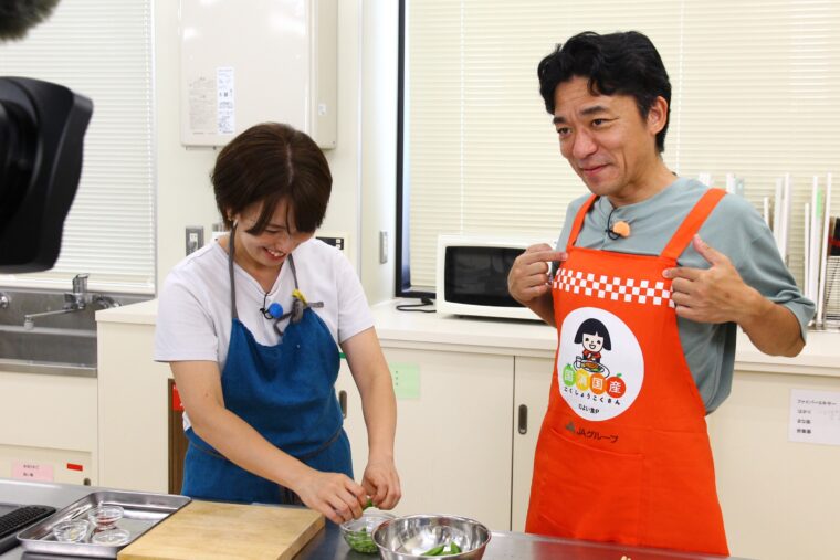 新デザインのエプロンをカメラマンにアピールする飛田アナ