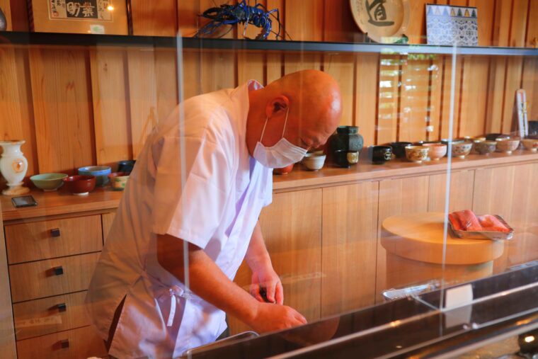 カウンター越しに料理の仕上げに向かう店主の黒井修さん