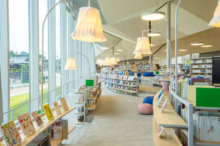 湾曲した書架が並ぶ、こどもとしょかん。照明は天井と同じ和紙でできている