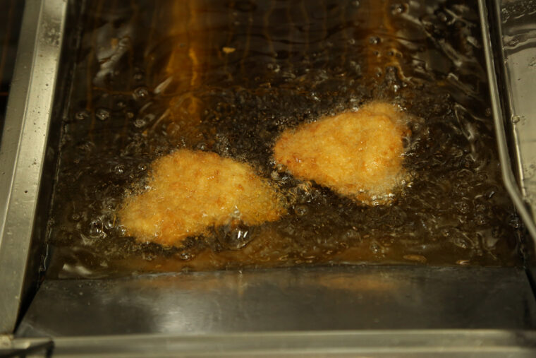 衣をまぶしたロース肉を、いい油（企業秘密）でジュワッと揚げます