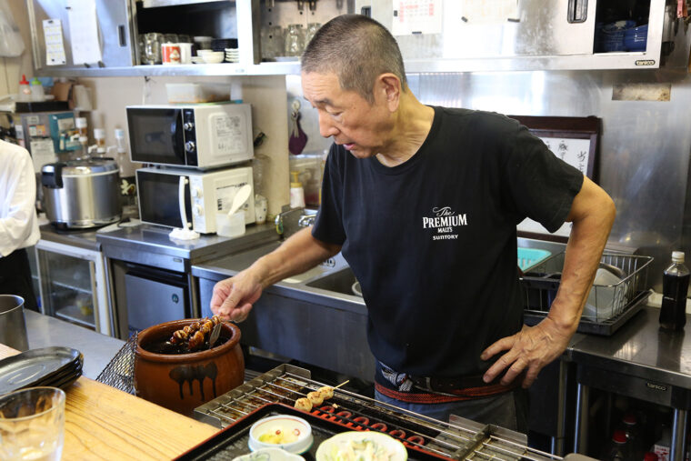 ふっくらと焼き上げた鶏モモとつくねをこだわりのタレにくぐらせる店主・青島さん