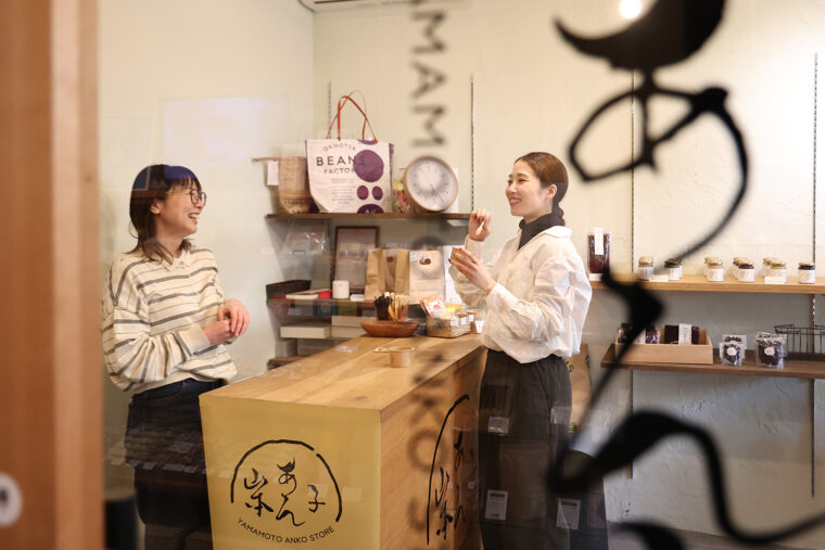 お土産に買って帰る商品を決めるため試食中のさくらさん。左がスタッフの山本淳子さん