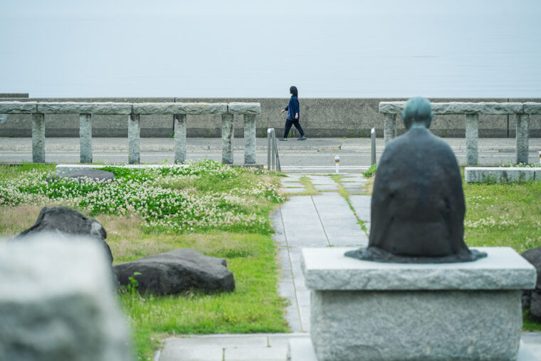 海辺を歩いている人々を良寛さんが見守っています
