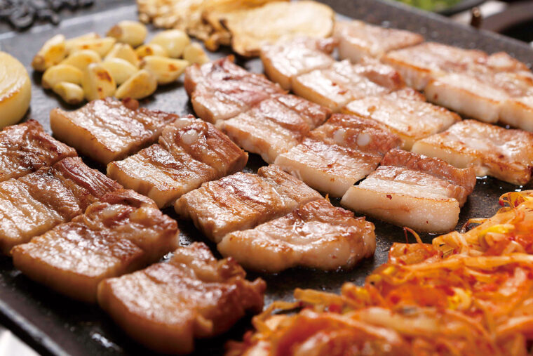韓国グルメの大定番、サムギョプサル。厚切りの豚バラ肉を鉄板で焼き、サンチュやエゴマの葉で巻いて食べる